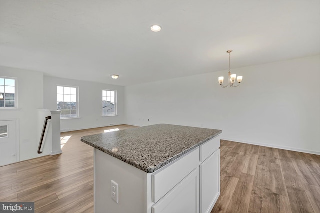 kitchen featuring light hardwood / wood-style flooring, white cabinets, dark stone counters, and decorative light fixtures