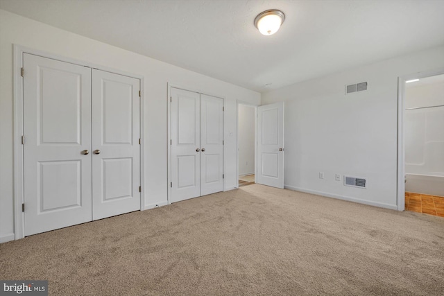 unfurnished bedroom with carpet flooring, connected bathroom, and two closets