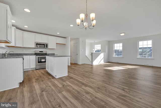 kitchen featuring appliances with stainless steel finishes, an inviting chandelier, light hardwood / wood-style flooring, white cabinets, and hanging light fixtures