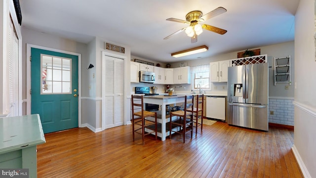 kitchen with sink, ceiling fan, light wood-type flooring, white cabinetry, and stainless steel appliances