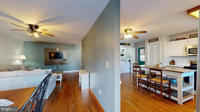 kitchen with range with electric cooktop, light hardwood / wood-style floors, ceiling fan, washer / clothes dryer, and white cabinetry