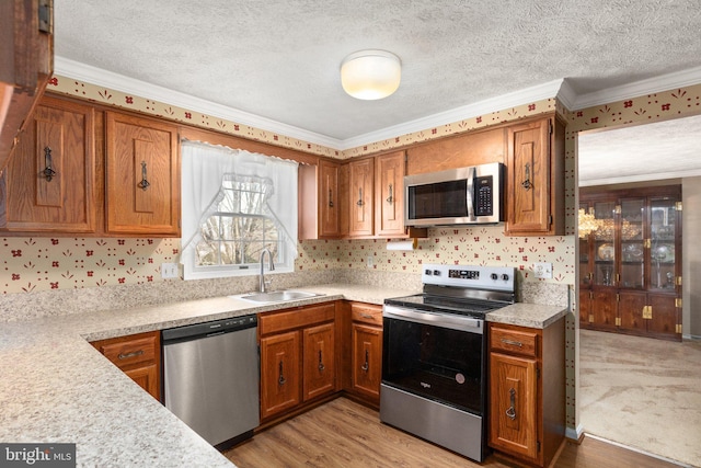 kitchen with sink, stainless steel appliances, light hardwood / wood-style flooring, crown molding, and a textured ceiling