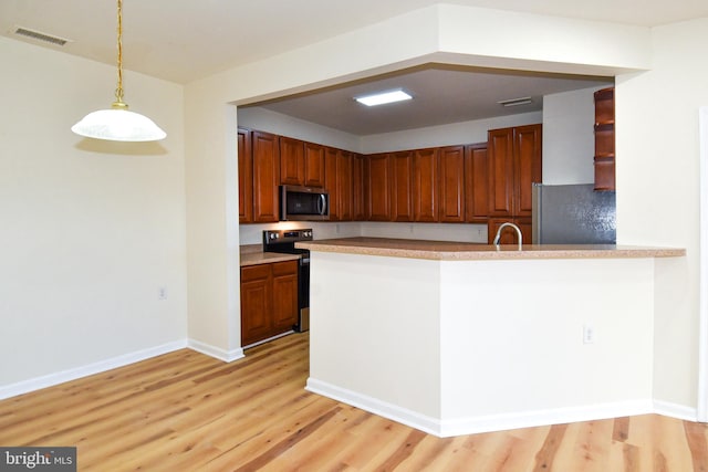 kitchen with sink, stainless steel appliances, kitchen peninsula, pendant lighting, and light wood-type flooring