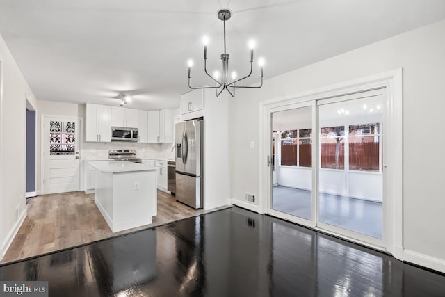 kitchen featuring appliances with stainless steel finishes, a kitchen island, pendant lighting, light hardwood / wood-style floors, and white cabinetry