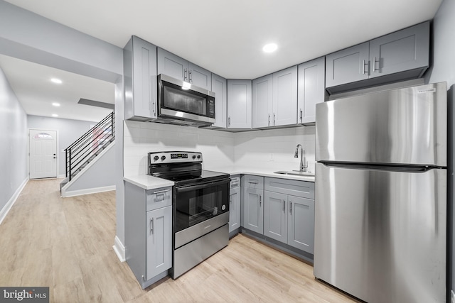 kitchen with stainless steel appliances, sink, light hardwood / wood-style flooring, backsplash, and gray cabinetry