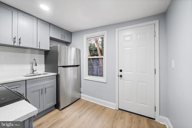 kitchen with sink, light hardwood / wood-style floors, decorative backsplash, stainless steel fridge, and gray cabinetry