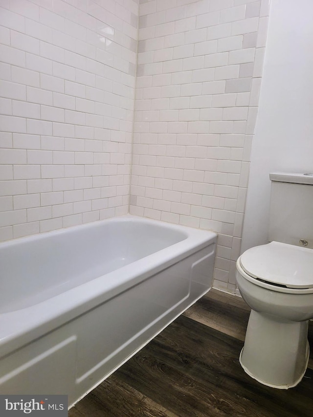 bathroom with hardwood / wood-style floors, toilet, and tiled shower / bath