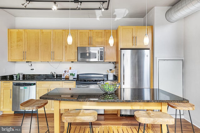 kitchen with a kitchen bar, appliances with stainless steel finishes, sink, wood-type flooring, and hanging light fixtures