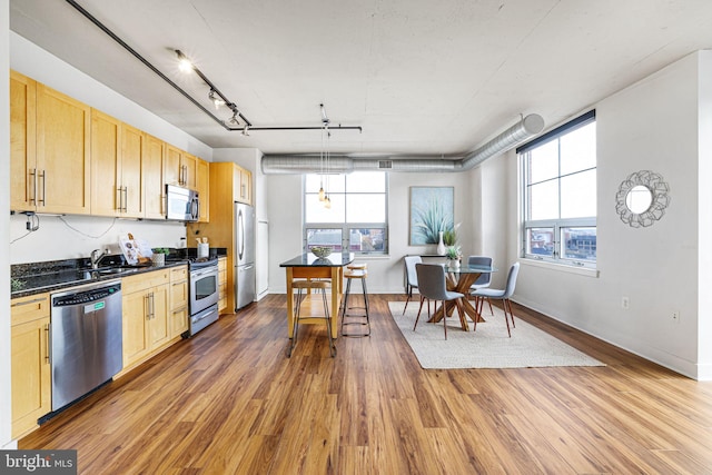 kitchen with light brown cabinets, dark hardwood / wood-style floors, pendant lighting, track lighting, and appliances with stainless steel finishes