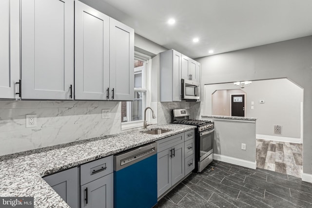 kitchen with light stone countertops, appliances with stainless steel finishes, backsplash, sink, and gray cabinets