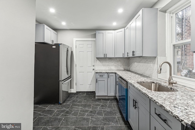 kitchen with gray cabinetry, sink, decorative backsplash, light stone countertops, and stainless steel appliances