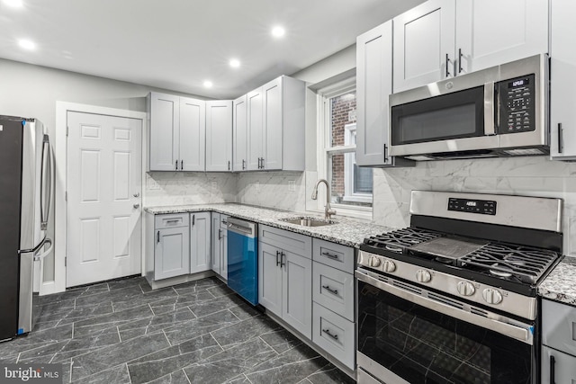 kitchen with sink, decorative backsplash, gray cabinets, light stone countertops, and appliances with stainless steel finishes