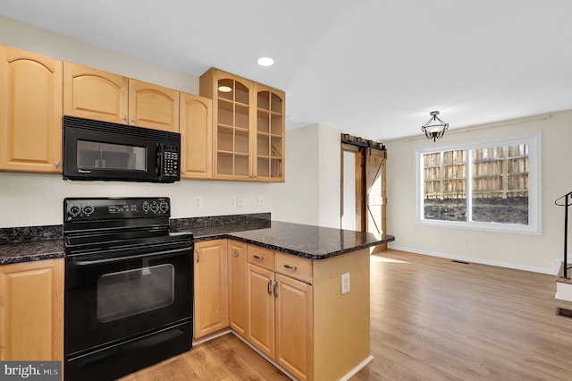 kitchen with light brown cabinets, black appliances, dark stone countertops, light wood-type flooring, and kitchen peninsula