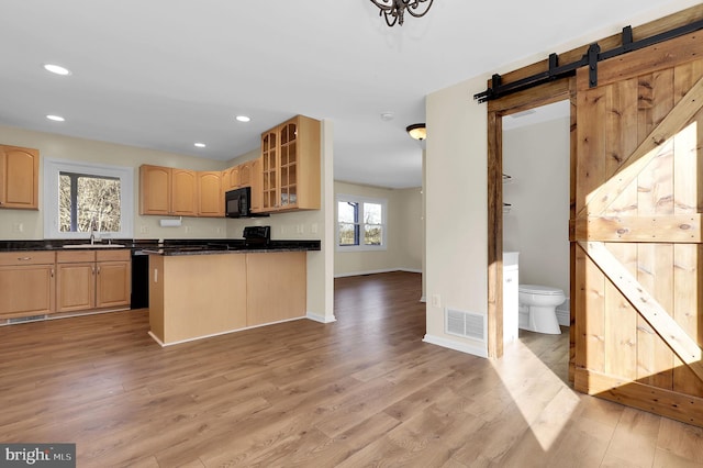 kitchen with black appliances, sink, a barn door, light wood-type flooring, and light brown cabinetry