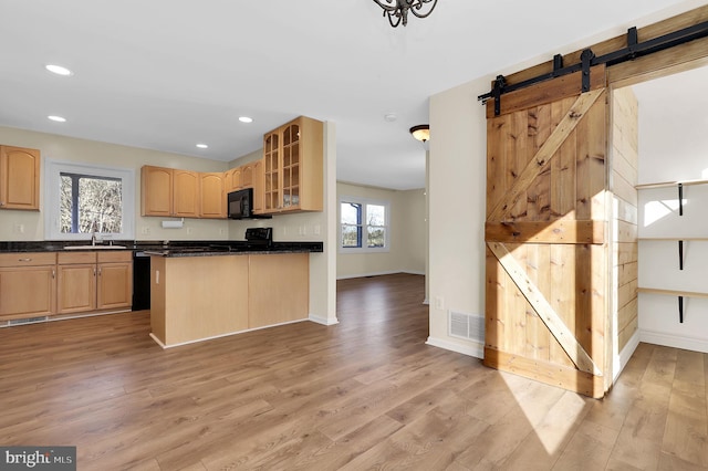 kitchen with black appliances, a barn door, light brown cabinetry, and light hardwood / wood-style flooring