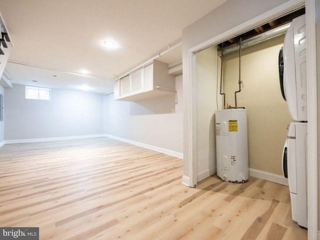 basement with water heater, stacked washing maching and dryer, and light wood-type flooring