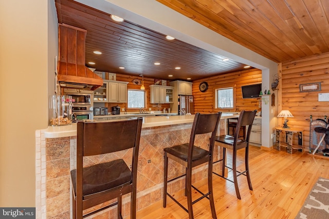 kitchen with log walls, cream cabinetry, light hardwood / wood-style floors, wood ceiling, and stainless steel appliances