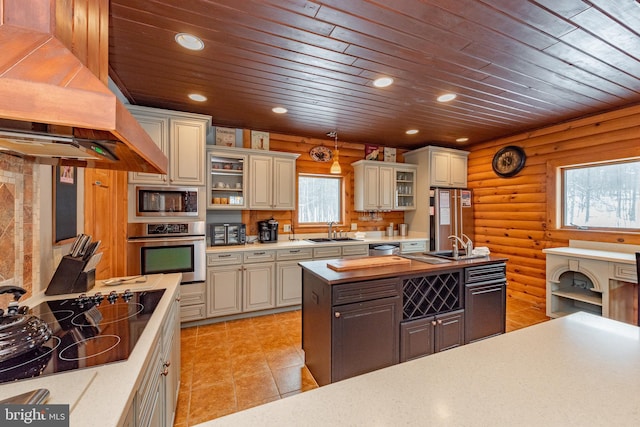 kitchen featuring premium range hood, stainless steel appliances, sink, log walls, and decorative light fixtures