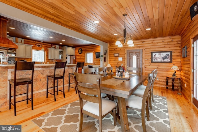 dining area with a notable chandelier, wooden ceiling, rustic walls, and light hardwood / wood-style flooring