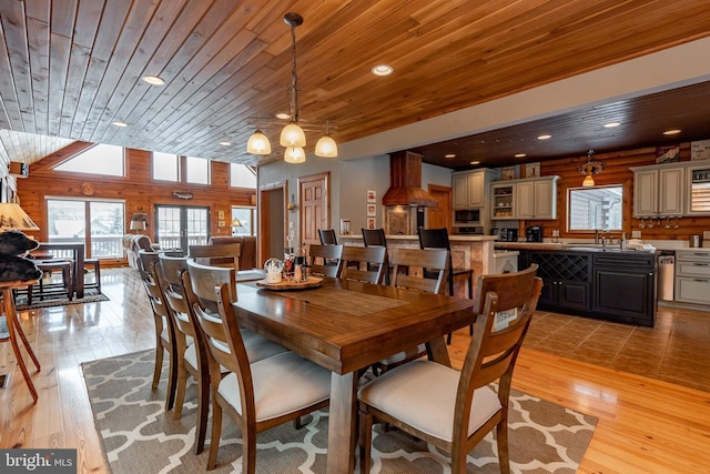 dining room featuring sink, wooden ceiling, light hardwood / wood-style flooring, lofted ceiling, and wooden walls