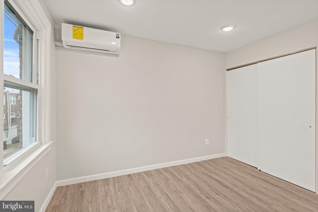 unfurnished bedroom featuring a wall mounted air conditioner, light hardwood / wood-style flooring, and a closet