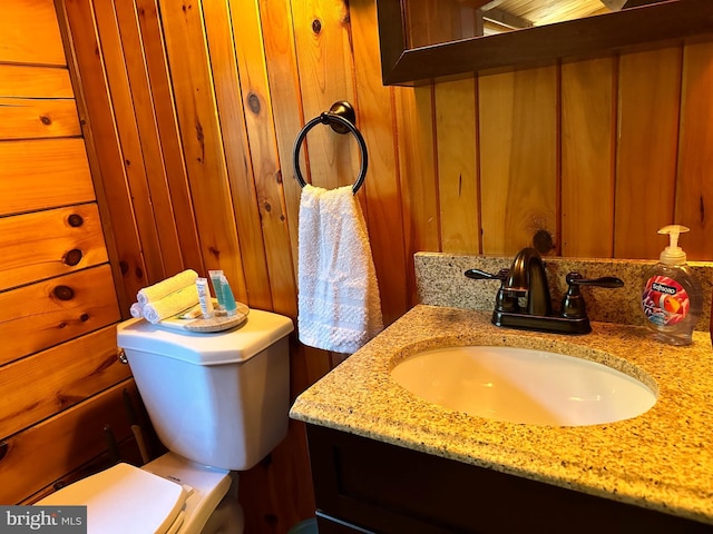 bathroom with vanity, toilet, and wood walls