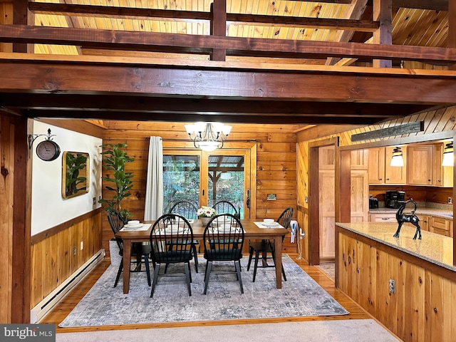 dining room featuring an inviting chandelier, wooden walls, beam ceiling, a baseboard radiator, and light hardwood / wood-style floors