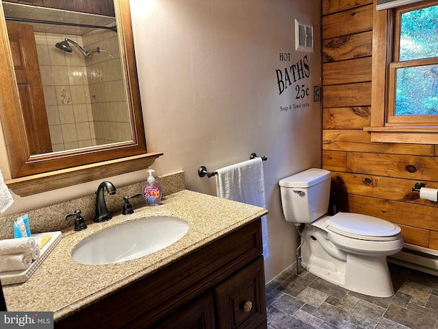 bathroom with a tile shower, wood walls, vanity, and toilet