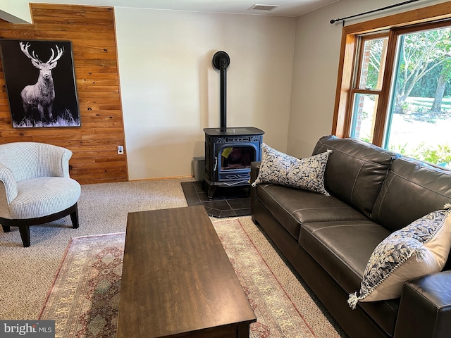 carpeted living room with a wood stove and wooden walls