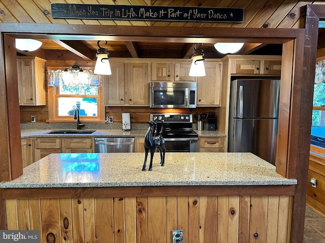 kitchen with light stone countertops, sink, stainless steel appliances, and decorative light fixtures