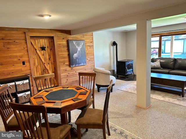 dining space featuring carpet, wood walls, and a wood stove