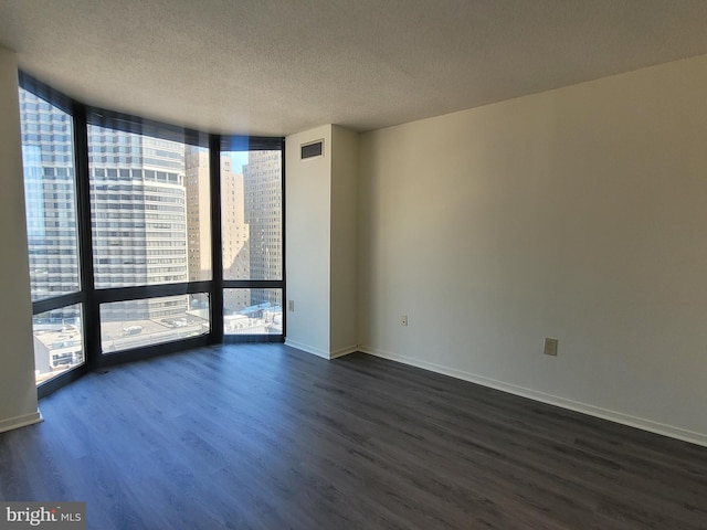 empty room with dark hardwood / wood-style flooring, a wall of windows, and a textured ceiling