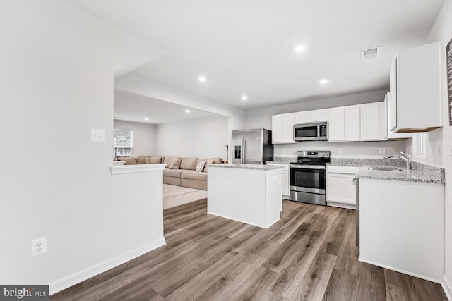 kitchen with a center island, sink, appliances with stainless steel finishes, white cabinets, and hardwood / wood-style flooring