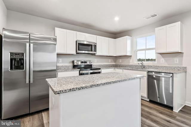 kitchen featuring appliances with stainless steel finishes, sink, wood-type flooring, a center island, and white cabinetry