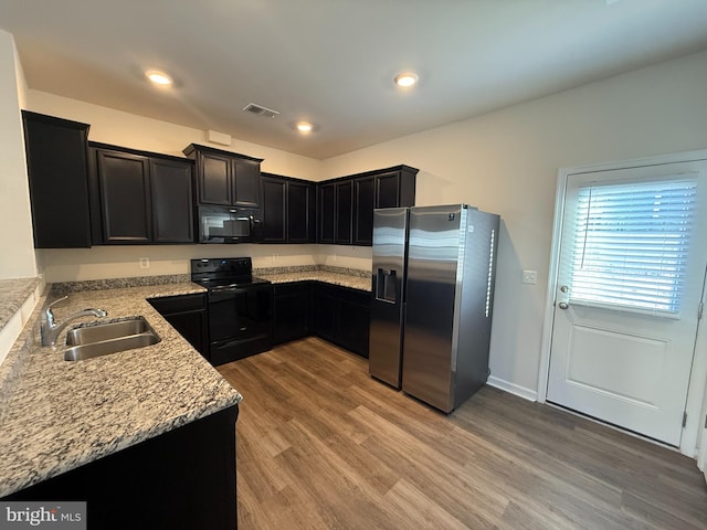 kitchen featuring sink, light hardwood / wood-style floors, light stone counters, and black appliances