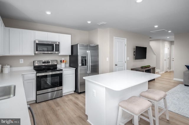 kitchen featuring appliances with stainless steel finishes, light wood-type flooring, a breakfast bar, a kitchen island, and white cabinetry