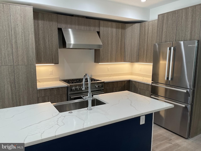 kitchen featuring light stone countertops, stainless steel appliances, sink, wall chimney range hood, and light hardwood / wood-style floors