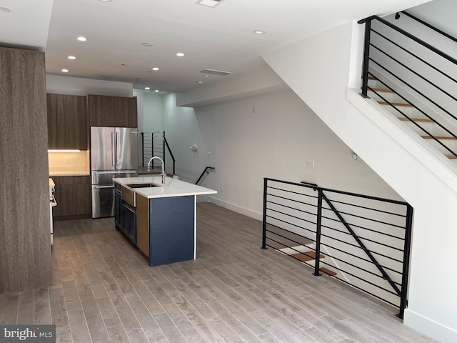 kitchen featuring stainless steel fridge, a kitchen island with sink, light hardwood / wood-style flooring, and sink