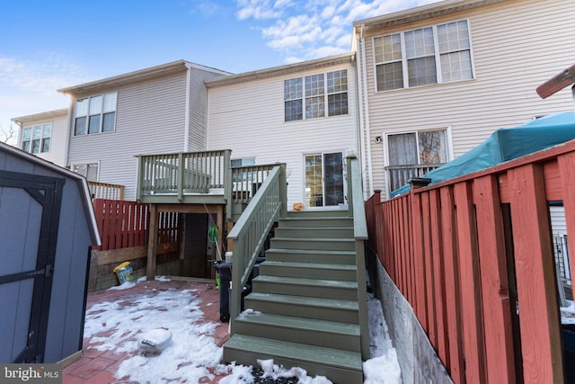 snow covered back of property featuring a wooden deck and a storage shed