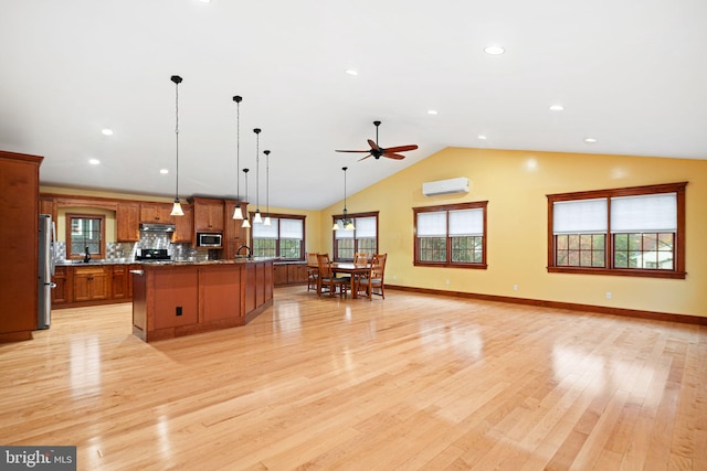 kitchen featuring light wood-type flooring, stainless steel appliances, ceiling fan, a center island with sink, and hanging light fixtures