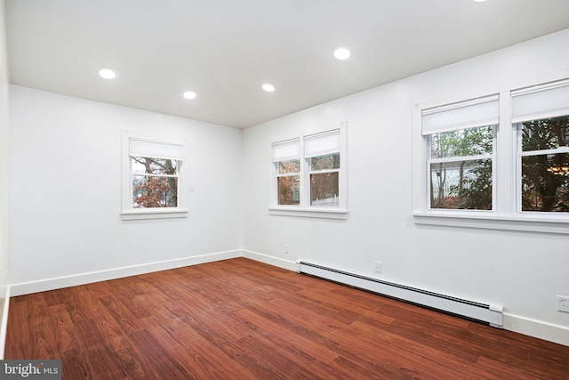 unfurnished room featuring hardwood / wood-style flooring, a healthy amount of sunlight, and a baseboard heating unit