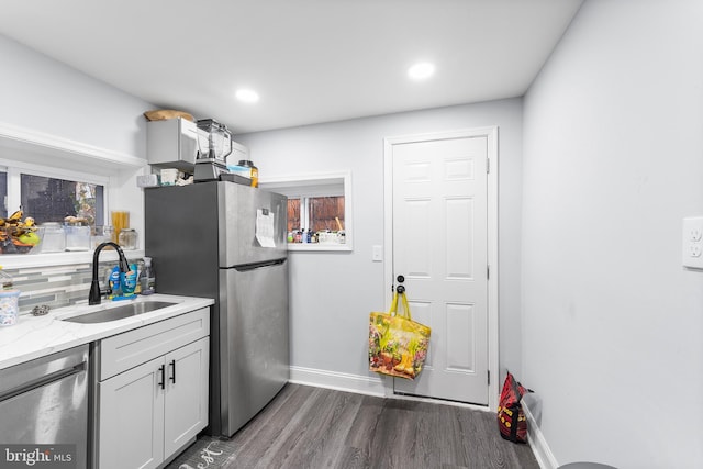 kitchen with appliances with stainless steel finishes, dark wood-type flooring, light stone counters, sink, and backsplash