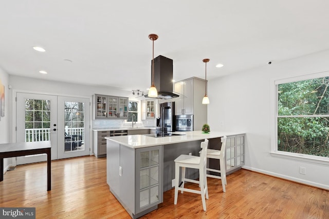 kitchen featuring kitchen peninsula, gray cabinetry, island range hood, decorative light fixtures, and light hardwood / wood-style flooring