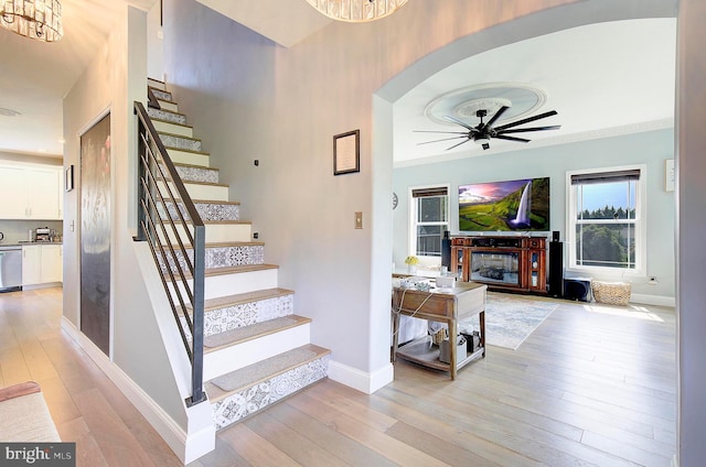 stairway featuring hardwood / wood-style floors, ceiling fan with notable chandelier, and crown molding