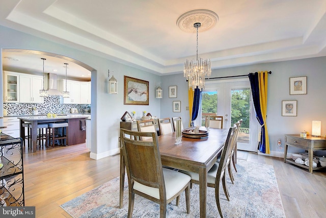 dining area with a chandelier, french doors, light wood-type flooring, and a tray ceiling