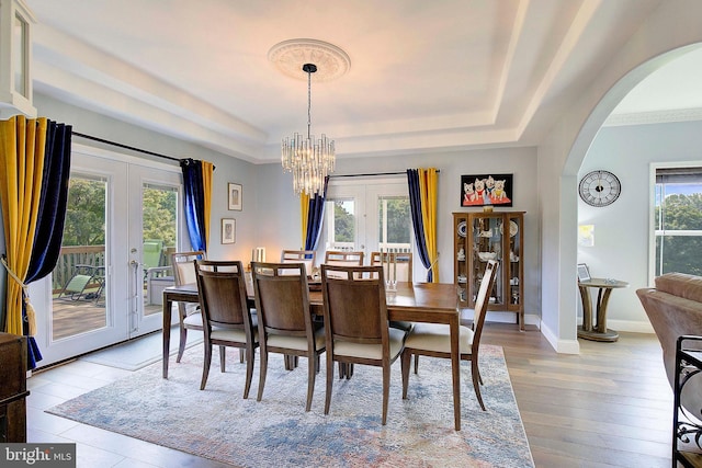 dining room featuring a chandelier, french doors, light wood-type flooring, and a raised ceiling