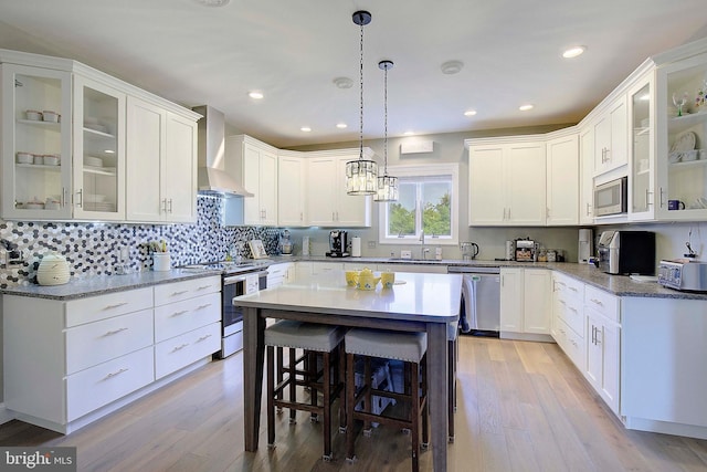 kitchen featuring white cabinets, appliances with stainless steel finishes, light wood-type flooring, and wall chimney exhaust hood