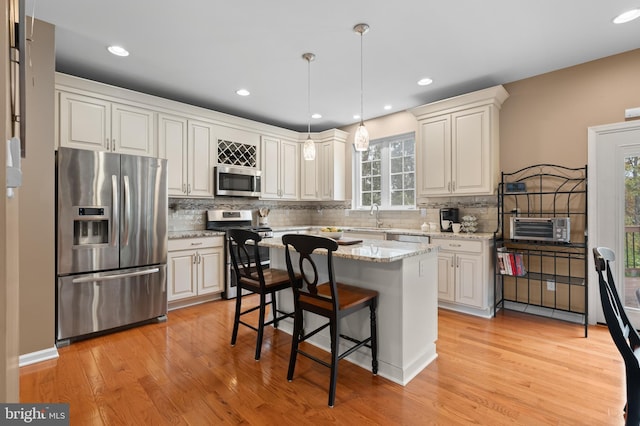 kitchen featuring pendant lighting, light hardwood / wood-style flooring, appliances with stainless steel finishes, a kitchen island, and a kitchen bar