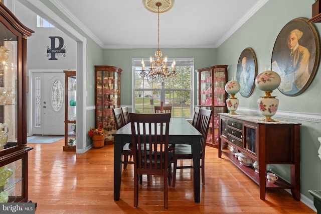 dining room with light wood-type flooring, ornamental molding, and an inviting chandelier