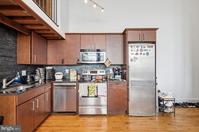 kitchen featuring sink, stainless steel appliances, tasteful backsplash, dark stone countertops, and light wood-type flooring